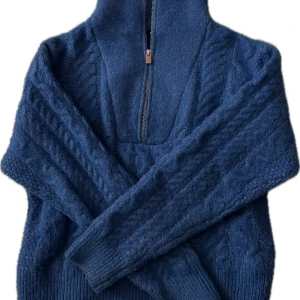 Blå stickad tröja med dragkedja - Säljer en snygg blå stickad tröja med dragkedja och hög krage. Tröjan har ett flätat mönster och långa ärmar, perfekt för kyliga dagar. Passar bra till både jeans och kjol. Perfekt för höst och vinter!