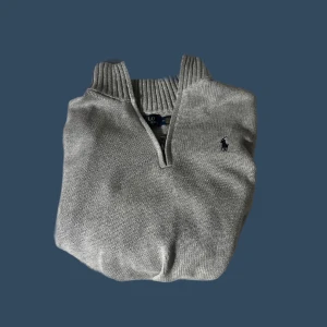 Grå stickad tröja från Polo Ralph Lauren - Säljer en snygg grå stickad tröja från Polo Ralph Lauren. Den har en dragkedja vid halsen och det klassiska logotypbroderiet på bröstet. Perfekt för kyliga dagar och ger en stilren look. Passar både till vardags och lite finare tillfällen.