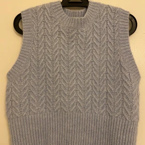 Ljusblå stickad väst från Zara - Säljer en ljusblå stickad väst från Zara med ett snyggt mönster. Västen har en ribbad nederkant och är perfekt för lager-på-lager-stil. Den är mjuk och bekväm, idealisk för kyligare dagar.