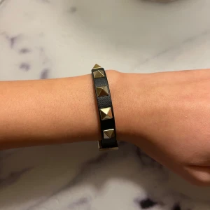 Svart armband med nitar från Valentino - Snyggt svart armband från Valentino Garavani med guldiga pyramidformade nitar. Kommer tyvärr aldrig till användning längre, använt ett fåtal gånger 