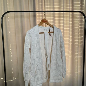 Vit stickad kofta med knytband - Säljer en vit stickad kofta med ett fint mönster och knytband i midjan. Koftan har långa ärmar och är perfekt för en mysig dag. Passar bra till både jeans och klänning.