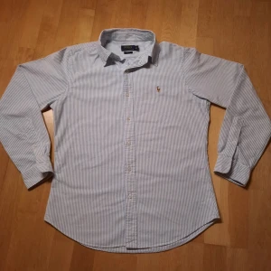 Ralph lauren skjorta - Ralph lauren skjorta gjord av bomull i blå och vit färg. Skjortan har inga stora skador och ser ut som ny.