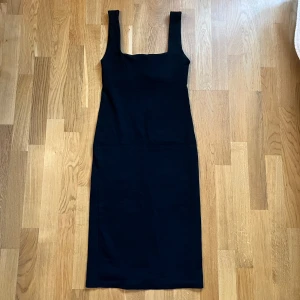 Svart klänning - Snygg svart klänning med breda axelband och en stilren design. Perfekt för en elegant look. Klänningen har en figurnära passform och är knälång.