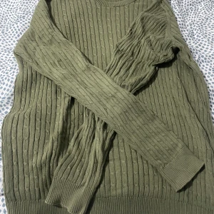 Olivgrön stickad tröja från Club XPRS - Säljer en olivgrön stickad tröja från Club XPRS. Tröjan har ett ribbat mönster och långa ärmar, perfekt för kyligare dagar. Den är både stilren och bekväm, idealisk för en avslappnad look.