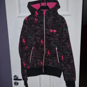 Mönstrad softshelljacka från KappAhl - Cool softshelljacka från KappAhl med ett unikt mönster i svart och rosa. Jackan har en dragkedja framtill och en huva med rosa foder. Sparsamt använd,  är som ny.