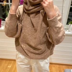 Beige stickad polotröja - Mysig beige stickad polotröja med långa ärmar och en hög krage. Perfekt för kyliga dagar och ger en avslappnad look. Tröjan har en loose passform och ribbade detaljer vid ärmslut och nederkant.