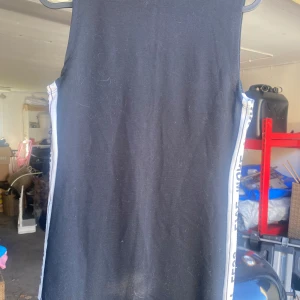 Svart ärmlös klänning från Pull&Bear - Säljer en cool svart ärmlös klänning från Pull&Bear. Den har vita sidopaneler med texten 'LIVE MORE WORRY LESS' vilket ger en sportig touch. Perfekt för en avslappnad dag eller en sommarfest. Klänningen är i nyskick och redo för nya äventyr!