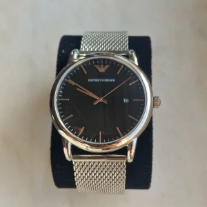 Emporio Armani klocka med svart urtavla - Säljer en stilren Emporio Armani klocka med en elegant svart urtavla och silverfärgade detaljer. Klockan har ett mesh-armband i rostfritt stål som ger en modern och lyxig känsla. Perfekt för både vardag och fest. Kommer i originalförpackning med instruktioner.