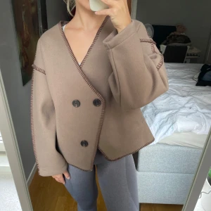 Brun kort kappa - Superfin beige/brun kort kappa, med stora svarta knappar. HELT NY, utan prislapp. Den har en lite oversized passform och fickor. Mjukt material och har snygga detaljer med synliga sömmar. Perfekt för höst och vår! Storlek: Small. 