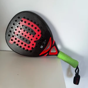 Wilson Bela team paddelrack - Wilson Bela team paddelrack. Racket är i bra skick med några kantstötningar som framgår på bilden, inget som påverkar spelet utan bara de estetiska. Nypris 1899kr
