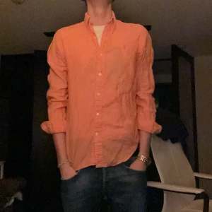 Orange Ralph Lauren linne skjorta - Säljer en snygg orange skjorta från Ralph Lauren i bomull. Skjortan har långa ärmar och klassiska knappar framtill. Perfekt för både vardag och fest! Den har en broderad logga på bröstet som ger en extra touch av stil. Passar bra till jeans eller chinos. Hör av dig vid intresse! 🧡