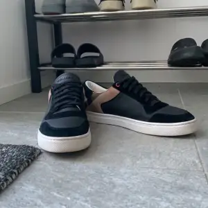 Säljer ett par snygga svarta sneakers från Burberry i skick 8/10. De har en klassisk rutig detalj på hälen och är gjorda i skinn och mocka. Perfekta för både vardag och fest! Skriv för bilder, frågor mm!