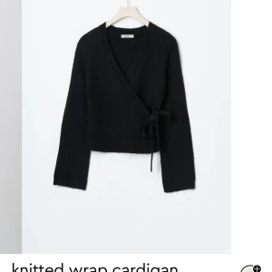 Svart omlott kofta - Säljer en stilren svart omlott kofta i stickat material. Perfekt för höst och vinter, med långa ärmar och knytning i sidan. Supermysig och lätt att matcha med olika outfits. Passar både till vardags och fest!