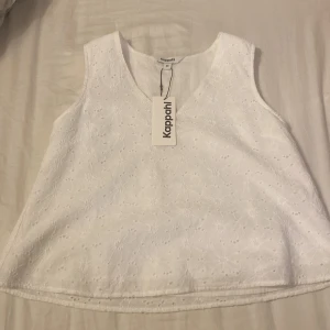 Vit ärmlös topp från Kappahl - Säljer en superfin vit ärmlös topp från Kappahl i storlek XS. Toppen har ett vackert broderat mönster och en v-ringad hals. Perfekt för sommardagar eller en avslappnad vårlook. Passar till ett par jeans, kostymbyxor och kjol. Den är helt ny och oanvänd med prislapp kvar!
