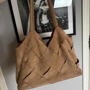 Väska - Säljer denna beiga tote bagen som har ett mockaliknande material. Den har en vävd design, ett huvudfack med en öppen innerficka och en innerficka med en gömd dragkedja🤎