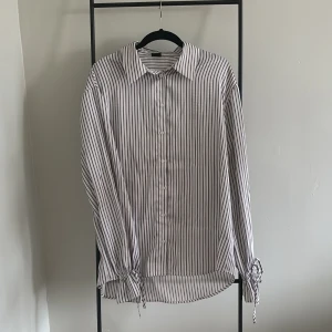 Randig skjorta från Gina Tricot - Stilren randig skjorta från Gina Tricot i storlek L. Skjortan har långa ärmar med knyt vid ärmsluten och klassisk krage.