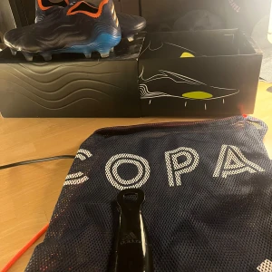Adidas Copa Sense fotbollsskor - Säljer ett par Adidas Copa Sense fotbollsskor i snyggt blått och orange. Skorna har en modern design med en vågig struktur och är perfekta för fotbollsspelare som vill ha både stil och funktion. De kommer med en praktisk förvaringspåse. Perfekt för både träning och match! Nästan helt oanvända. Skick 10/10 storlek 41