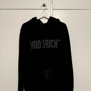 Svart hoodie från Hoodrich - Säljer en svart hoodie från Hoodrich i storlek L. Den har en stor logga på framsidan och coola detaljer på baksidan. Perfekt för höst och vinter.