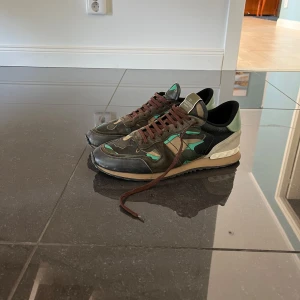Valentino Rockrunner  - Säljer ett par coola Valentino Rockrunner sneakers i camouflage. De har en unik mix av gröna och bruna nyanser med svarta detaljer. Skorna har snörning och är i bra skick, perfekta för en avslappnad men stilren look. Passar bra till både vardag och fest!