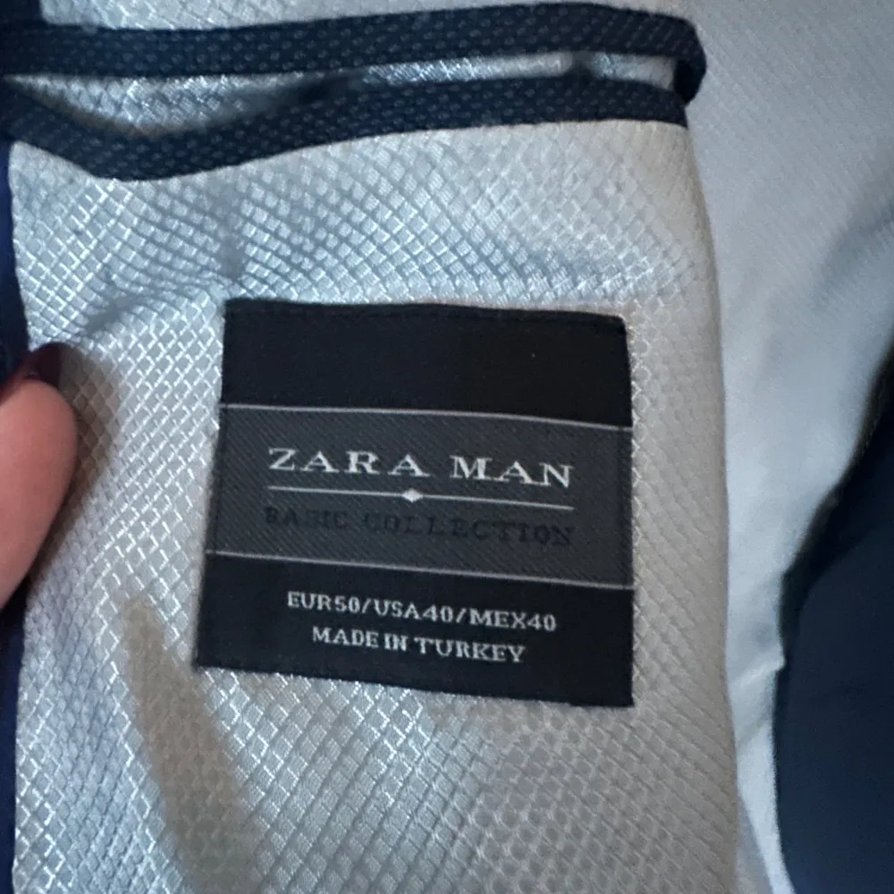 Säljer en stilren mörkblå kostym från Zara Man Basic Collection. Kavajen har en klassisk passform med två knappar och byxorna är raka och eleganta. Perfekt för både formella tillfällen och fest. I mycket bra skick. Passar utmärkt för alla årstider.. Kostymer.