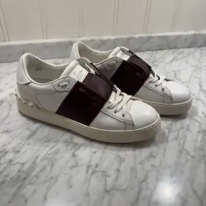 Säljer ett par snygga Valentino Garavani sneakers i vitt skinn med vinröda detaljer. Skorna har coola nitar runt hälen och en bred rem över snörningen. Använda men i bra skick, har tyvärr inte kvitto eller og saker för att min mamma hade inte sparat det men hör av dig vid intresse samt frågor, pris är ej hugget i sten😉🤩