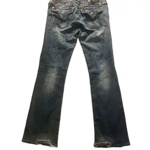 Säljer ett par blå miss me jeans med snygga slitningar och dekorativa detaljer på bakfickorna. Jeansen har en bootcut-stil och är i bra skick med lite slitage vid benslutet. strl 31 midja: 38 innerbenslängd: 85