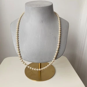 Klassiskt pärlhalsband med dekorativt lås - Säljer ett elegant pärlhalsband med vita pärlor och ett vackert, detaljerat lås i silverfärg. Perfekt för både vardag och festliga tillfällen. Halsbandet har en tidlös design som passar alla stilar. Ett måste för smyckesamlingen!