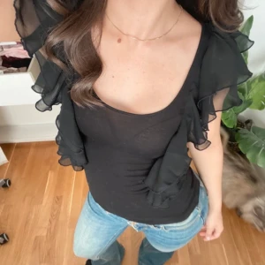 Svart topp med volanger - Snygg svart topp med volangdetaljer på ärmarna. Storlek s💕