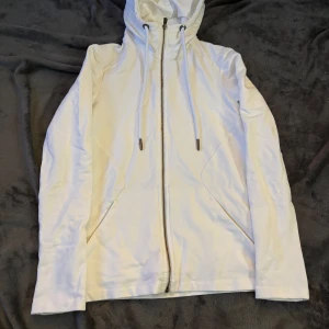 Vit jacka från Sail Racing - Säljer en snygg vit jacka från Sail Racing i damstorlek XS. Jackan har en dragkedja framtill och en praktisk huva med dragsko. Perfekt för vår och höst, med en stilren design som passar till det mesta. Den är i mycket bra skick och redo för nya äventyr!