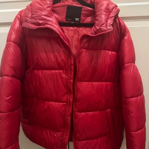 Röd pufferjacka från 157 - Säljer en snygg röd pufferjacka från 157 i storlek XS. Jackan har en dragkedja framtill och är perfekt för kyliga dagar. Den är i bra skick och supermysig att ha på sig. Passar perfekt till både höst och vinter!