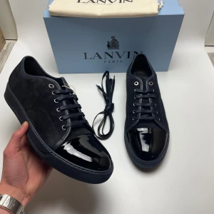 Lanvin skor(nya) - Säljer ett par stilrena svarta sneakers från Lanvin i nytt skick. Skorna har en snygg kombination av skinn och syntet med en glansig tå och klassisk snörning. Perfekta för både vardag och festliga tillfällen. Kommer med originalförpackning och extra skosnören. Uk12