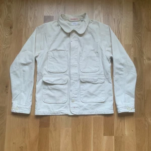 Vit jacka från Apolis - Säljer en stilren vit jacka från Apolis i storlek M. Jackan har långa ärmar och flera praktiska fickor framtill. Perfekt för vår och höst med sin klassiska design och bekväma passform. Passar både till vardags och lite finare tillfällen.