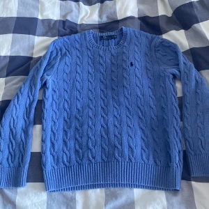 Blå stickad tröja från Ralph Lauren - Säljer en snygg blå stickad tröja från Ralph Lauren. Den har ett klassiskt flätmönster och en liten broderad logga på bröstet. Perfekt för kyliga dagar och passar både till vardags och lite finare tillfällen. Tröjan är i mycket bra skick och redo för en ny ägare! 💙