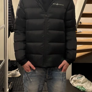 Svart dunjacka från Sail Racing - Säljer en svart dunjacka från Sail Racing i mycket bra skick. Jackan är långärmad och har en dragkedja framtill. Perfekt för kalla vinterdagar med sin pufferstil som håller värmen. Den har en normal passform och är riktigt snygg och stilren. Passar både till vardags och lite mer uppklädda tillfällen. Pris kan diskuteras!!!!
