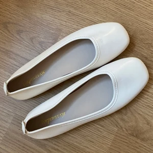 Vita ballerinaskor - Säljer ett par stilrena vita ballerinaskor i syntetmaterial. De har en klassisk design med rundad tå och låg klack, perfekt för både vardag och fest. Skorna är i mycket bra skick (aldrig använda) och passar till många olika outfits🤍