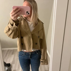 Beige croppad trenchcoat från Gina Tricot - Säljer en superfin beige croppad trenchcoat från Gina Tricot. Använd få tal gånger och super fin till våren\hösten