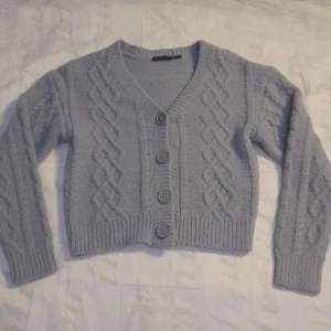 Grå kofta från xoxo friends - Säljer en superfin grå kofta från xoxo friends. Den är stickad med ett snyggt flätmönster och har stora knappar framtill. Koftan är croppad och har långa ärmar, perfekt för höst och vinter. Den är i mycket bra skick och redo för en ny ägare.Använd 2 gånger,den är för liten.