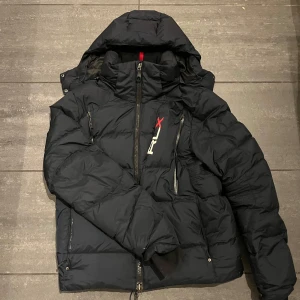 Svart pufferjacka från RLX - Säljer en svart pufferjacka från RLX i mycket bra skick. Jackan har en snygg och praktisk dragkedja framtill och en huva för extra värme. Perfekt för kalla vinterdagar. Den är långärmad och har en modern stil som passar både till vardags och utomhusaktiviteter. Väldigt bra skick och rekommenderar för 170-185 ungefär. 