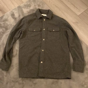 Grå overshirt från Kappahl - Säljer en stilren grå overshirt från Kappahl i storlek S. Den är tillverkad i 100% bomull och har långa ärmar med knappar framtill. Perfekt för höst och vår, och funkar både som jacka och skjorta. Två praktiska bröstfickor med knappar ger en snygg detalj. 🩶 Den är i nyskick inte använd pga av att den är lite stor!