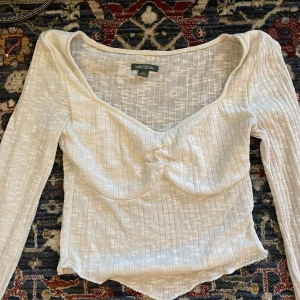 Vit ribbad topp från Wild Fable - Säljer en superfin vit ribbad topp från Wild Fable i storlek XS. Toppen har långa ärmar och en snygg v-ringad design med rynkdetalj framtill. Perfekt för både vardag och fest! 🕊️ Den har börja gå upp lite på två ställen, det syns i bilderna!