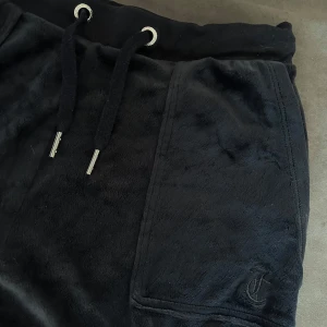 Mörkblåa byxor från Juicy Couture - Säljer ett par mörkblåa byxor från Juicy Couture i mjukt material. Köpte dem för 1500kr. De har en bekväm midja med snörning och praktiska fickor med knappar. Perfekta för en avslappnad stil eller mysiga dagar hemma. 💙