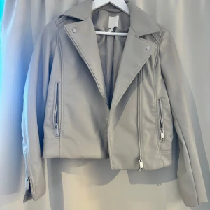 Beige skinnjacka från H&M - Säljer en snygg beige skinnjacka från H&M i storlek 34. Jackan har  dragkedjor och knappar. Perfekt för höst och vår, och funkar både till vardags och fest. Den är i mycket bra skick.