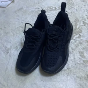 Svarta Nike sneakers - Säljer ett par svarta Nike sneakers i bra skick. De har en stilren design med snörning och en bekväm sula. Perfekta för både vardag och träning. Skorna är i syntetmaterial och har en modern look.