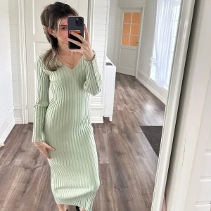 Ljusgrön ribbad klänning - Säljer en superfin ljusgrön ribbad klänning med lång ärm och v-ringning. Den är tight och figurnära, perfekt för både vår och höst. Klänningen har en stilren design med knappar på ärmarna som ger en extra touch. 