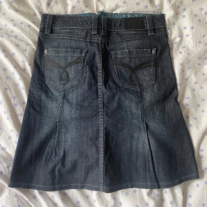 Jeanskjol med broderad detalj - Säljer en snygg jeanskjol i mörk denim med en cool broderad detalj på insidan av linningen. Kjolen har en klassisk femficksdesign och stängs med dragkedja och knapp framtill. Perfekt för en avslappnad vardagslook! Lågmidjad från Esprit.