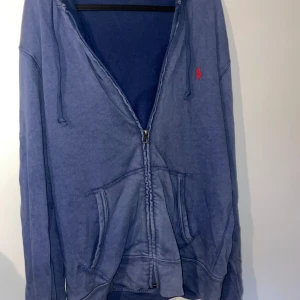 Blå hoodie från Ralph Lauren - Säljer en snygg blå hoodie i nyskick från Ralph Lauren. Den har en dragkedja framtill och en klassisk känguruficka. Perfekt för en avslappnad stil och passar bra till både jeans och joggers. Den är i bra skick och redo för en ny ägare!