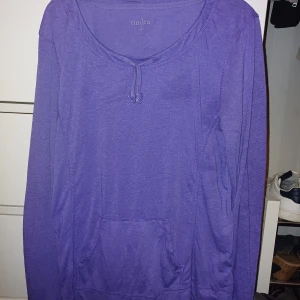Lila långärmad tröja från Tindra - Säljer en snygg lila långärmad tröja från Tindra. Den har en bekväm passform och en praktisk ficka framtill. Perfekt för en avslappnad stil eller mysiga dagar hemma. 💜