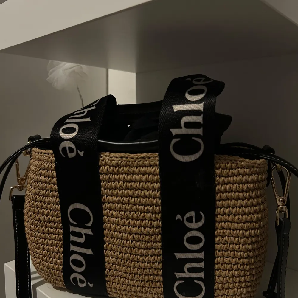 Säljer en superfin beige väska från Chloé. Den är gjord i ett flätat material som ger en snygg och somrig look. Väskan har svarta handtag med Chloé-loggan tryckt i vitt, vilket ger en cool kontrast. Perfekt för både vardag och fest!. Laukut & Käsilaukut.