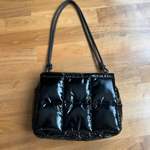 Axelväska  - Väska i blank svart färg, från hm men säljer då den aldrig kommit till användning. Rymlig väska med en ficka med dragkedja på insidan av väskan. Bra skick och inga defekter. 