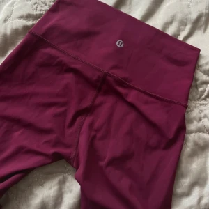 Vinröda leggings från Lululemon - Säljer ett par snygga vinröda leggings från Lululemon. De är högmidjade och perfekta för träning eller en chill dag hemma. Materialet är mjukt och stretchigt, vilket gör dem superbekväma att ha på sig. Passar perfekt för höst och vår!